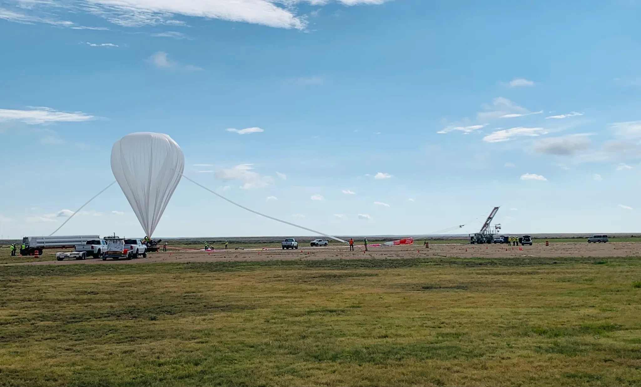 Atmospheric balloon being prepared for launch on an open field with ground crew